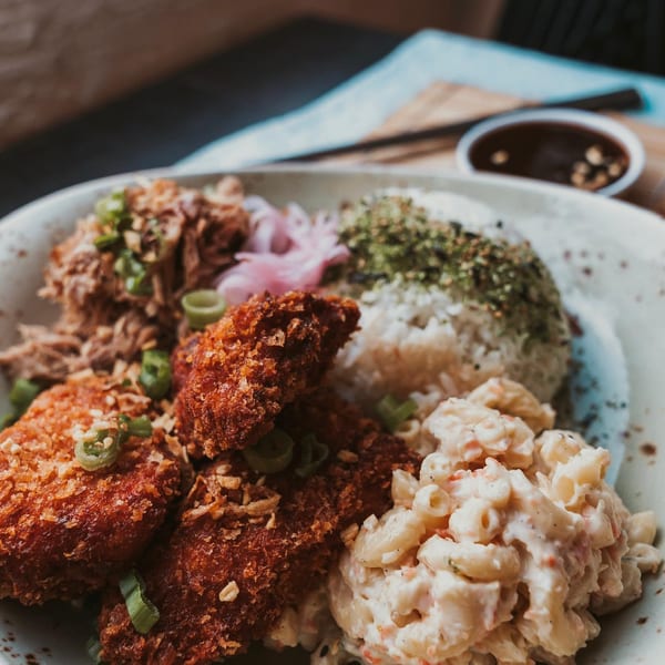 A close-up of a Hawaiian plate lunch with crispy fried chicken, pulled pork, macaroni salad, and rice.