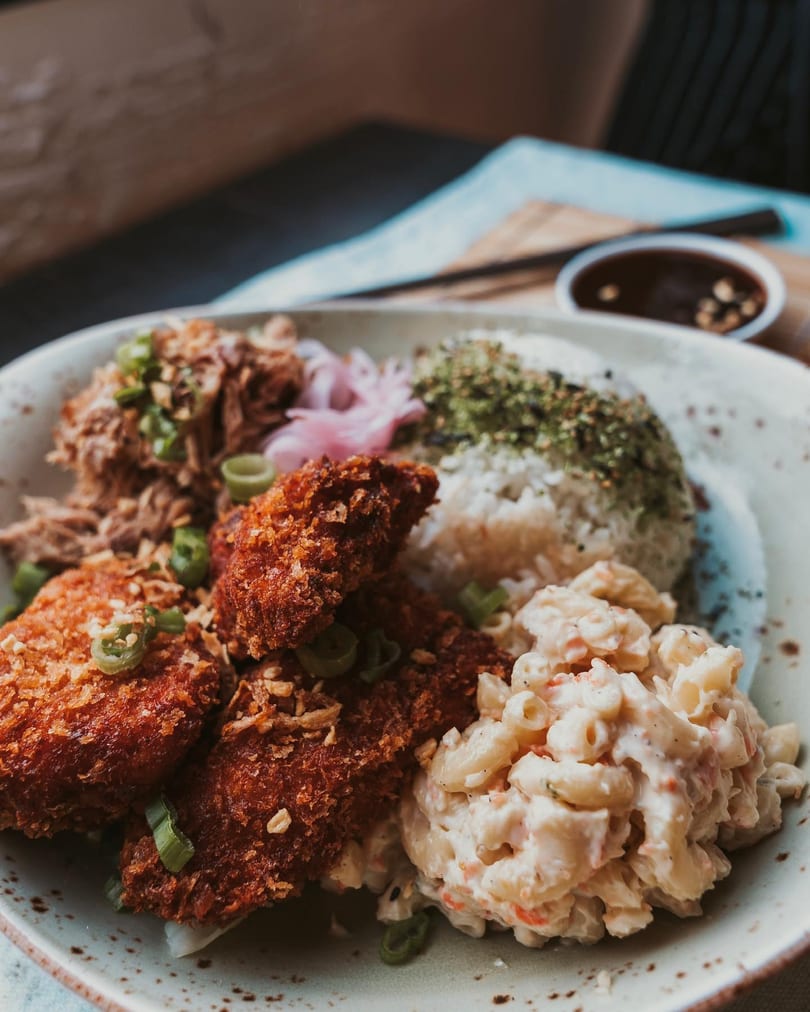 A close-up of a Hawaiian plate lunch with crispy fried chicken, pulled pork, macaroni salad, and rice.