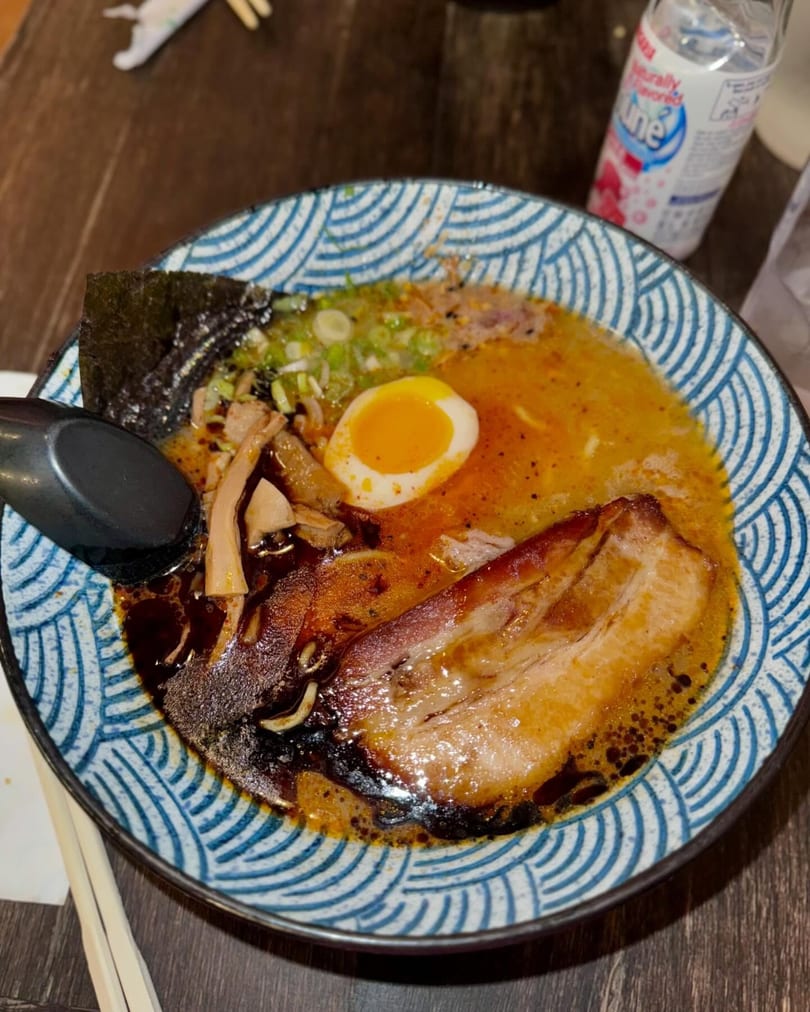 A bowl of ramen with pork belly, a soft-boiled egg, seaweed, and green onions.