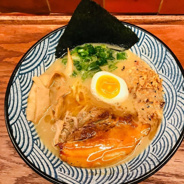 Ramen bowl with pork, egg, green onions, bamboo shoots, and nori on a patterned dish.